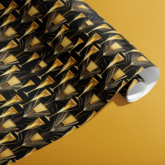 A partially unfurled roll of Flutes & Fans wrapping paper showing gilded fans and slender champagne flutes on a black ground, resting on a deep gold surface.