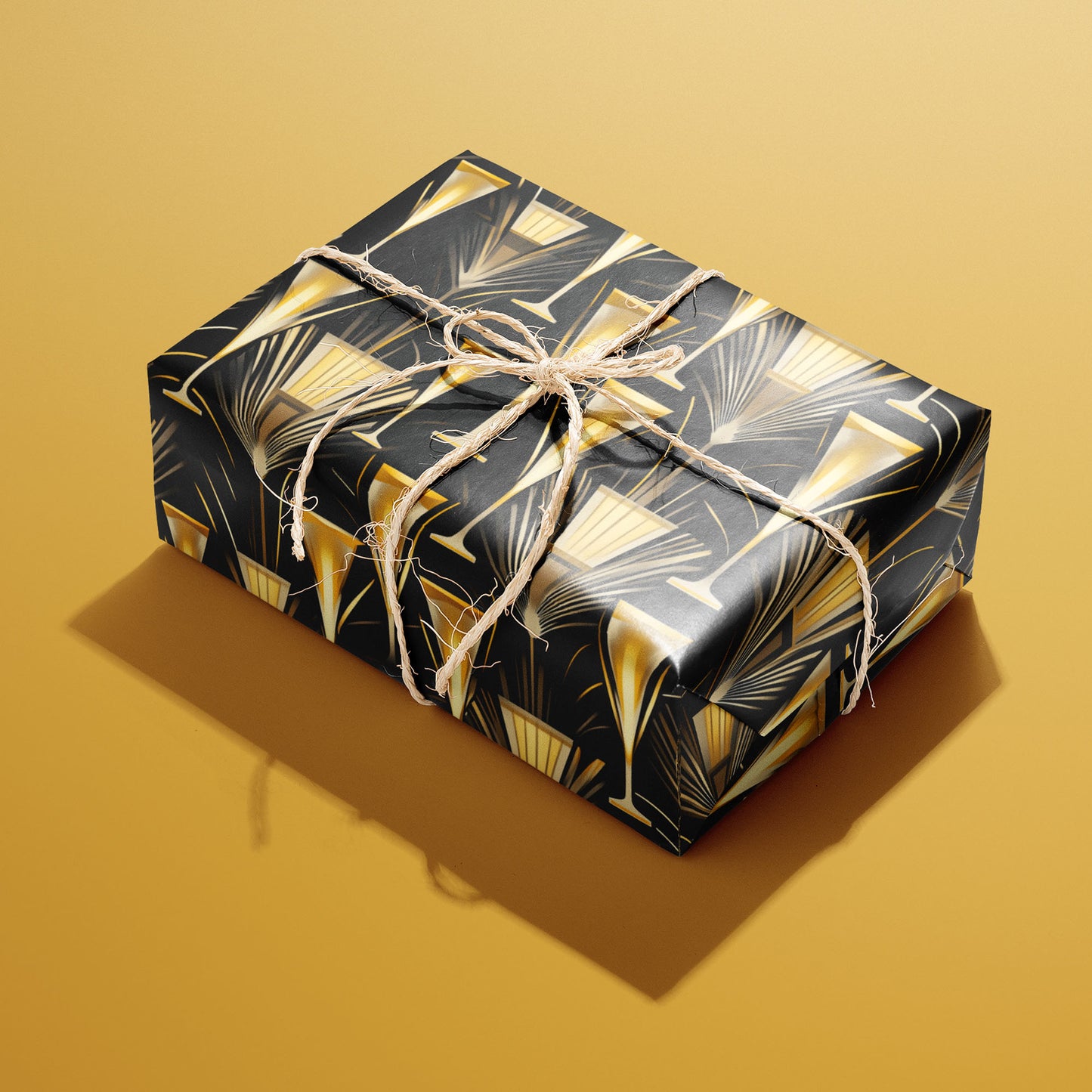 A single gift wrapped in Flutes & Fans and tied with natural twine, featuring art deco fanbursts and champagne flutes in soft gold on black, set on a gold background.