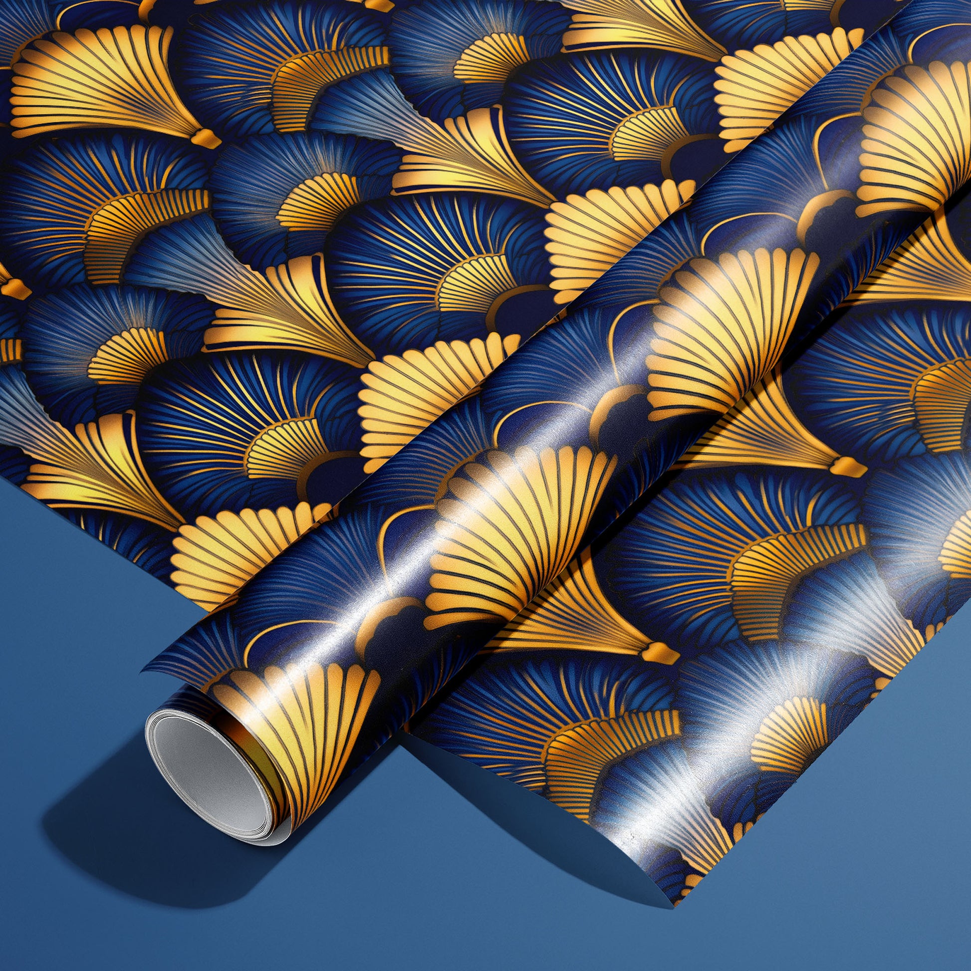 A roll of Gilded Ginko rests on a matching unrolled sheet, featuring gold and blue ginkgo leaves and fine stems, on a blue surface.