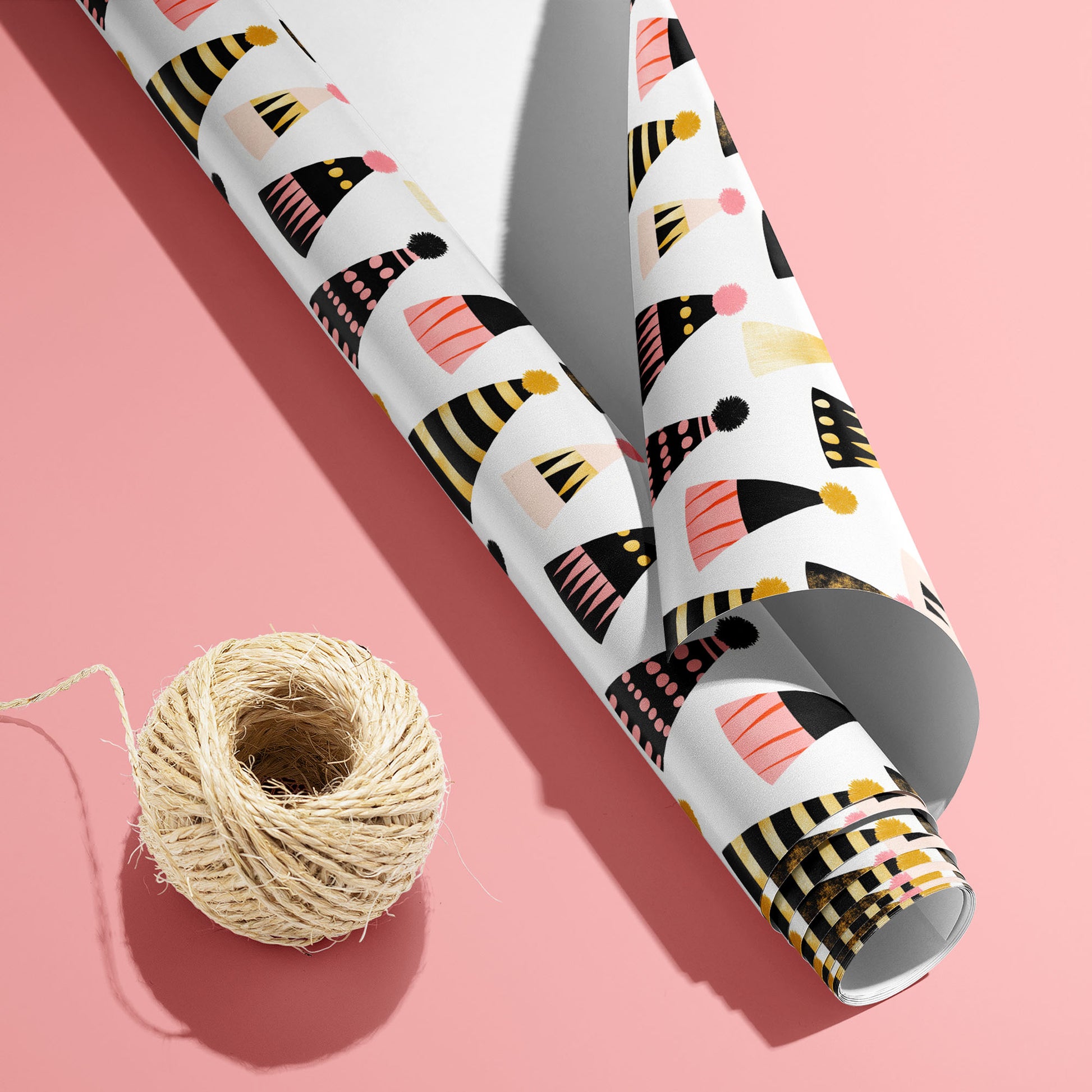 A partially unfurled Party Hat Parade roll with the white underside visible beside a spool of natural twine, featuring festive hats on a bright pink background.