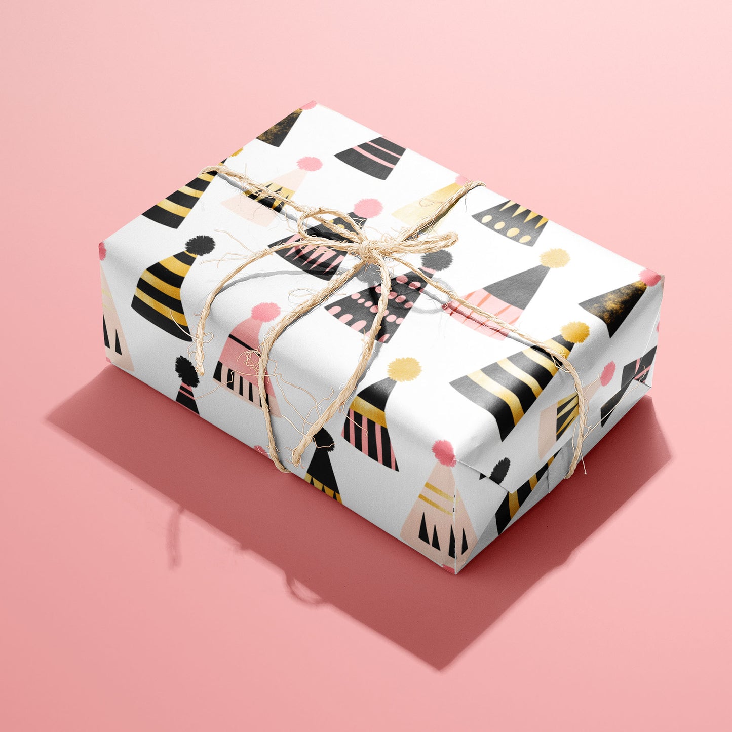 A single rectangular gift wrapped in Party Hat Parade paper—cheerful party hats with pom-poms—tied with natural twine on a bright pink background.
