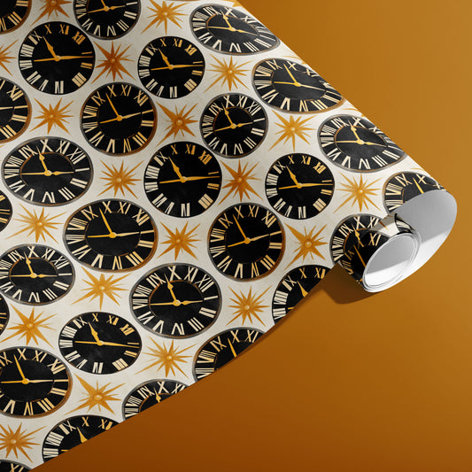 A partially unfurled roll of Deco Century wrapping paper reveals black clock dials and gold starbursts on pearl white, photographed on a golden mustard background.