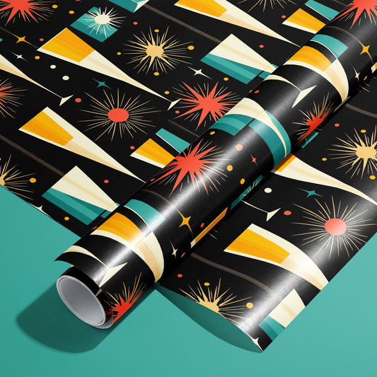A roll of Midcentury Starburst wrapping paper on an unrolled sheet, with atomic starbursts, champagne flutes, and confetti dots in red, gold, and teal on black, set on a teal surface.