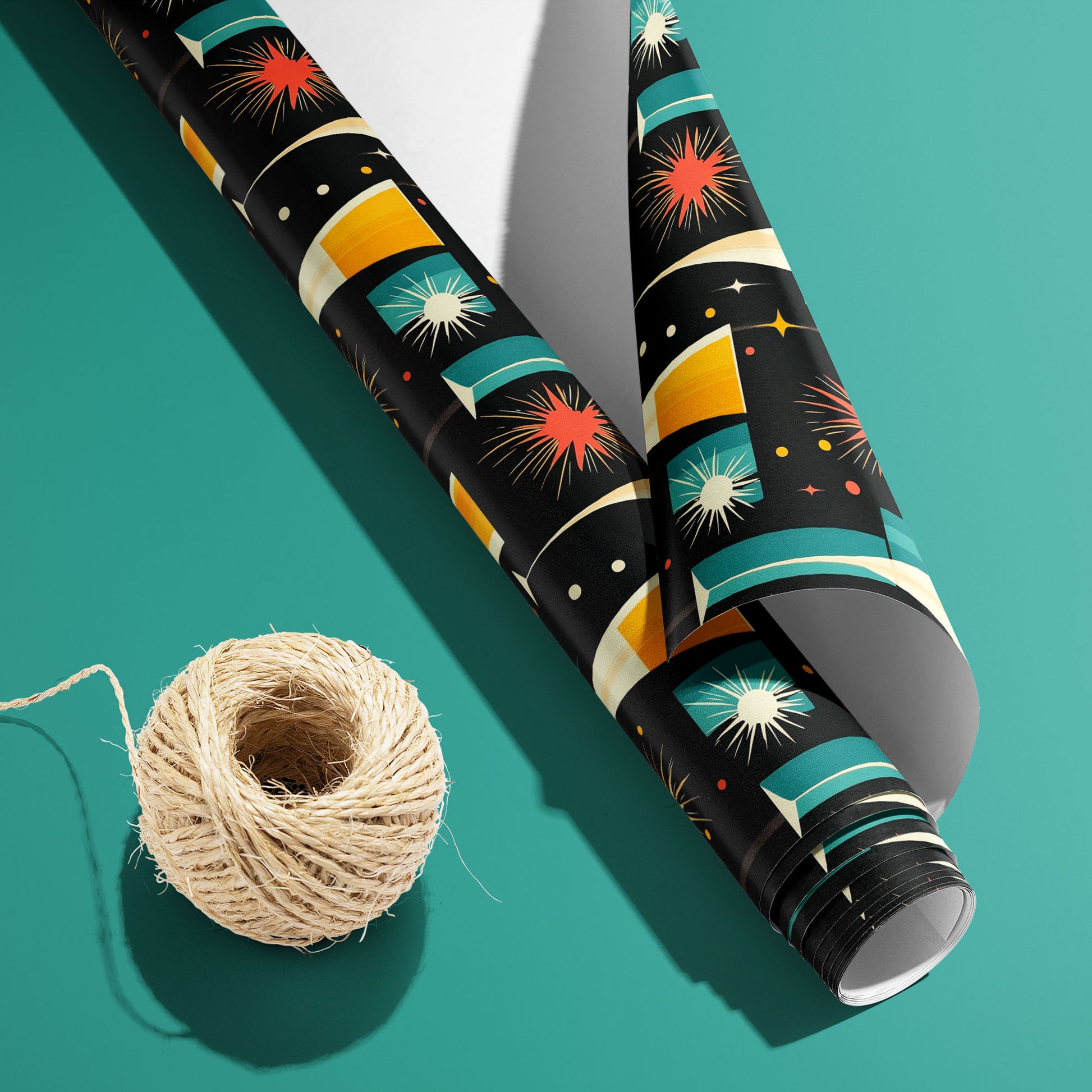 A partially unfurled roll of Midcentury Starburst with its white underside visible beside a spool of natural twine, featuring atomic starbursts and flutes on black over a teal surface.