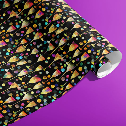 A partially unfurled roll of Radiant Revelry wrapping paper reveals iridescent champagne flutes with rainbow bubbles on black against a vibrant purple background.