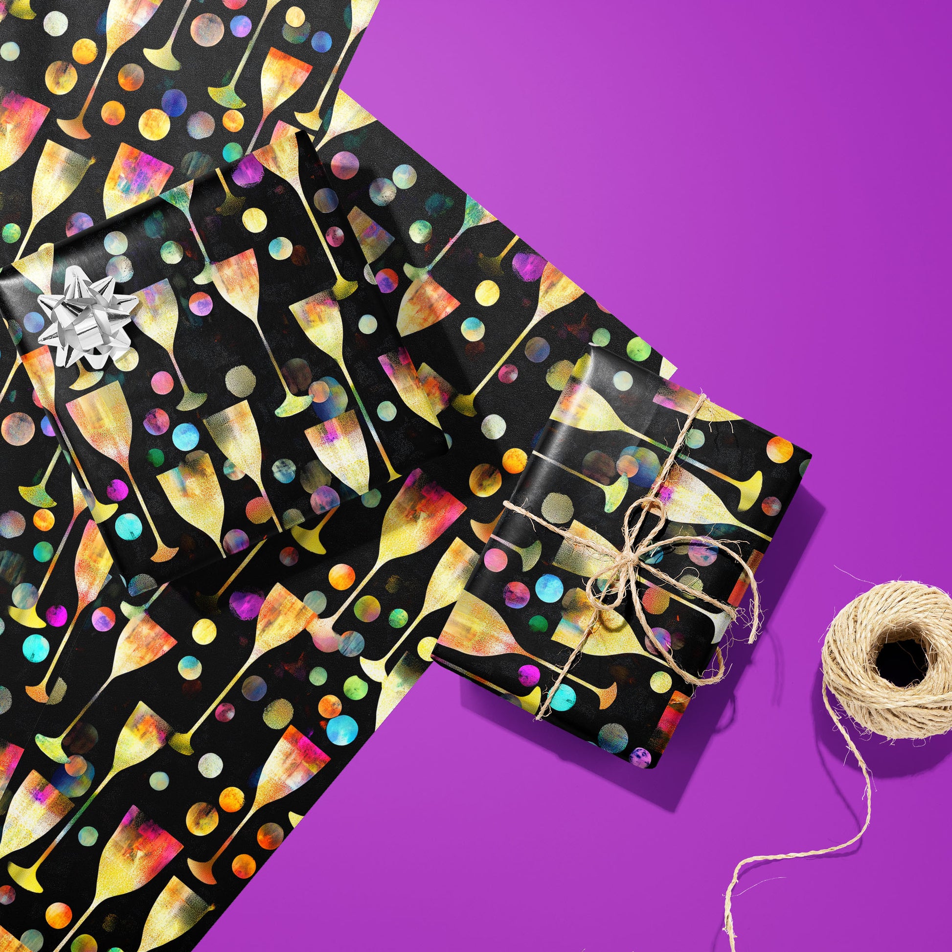 Two gifts in Radiant Revelry paper—one with a silver bow and one tied with twine—rest on unused sheets with champagne flutes and colorful bubbles beside twine on a purple background.