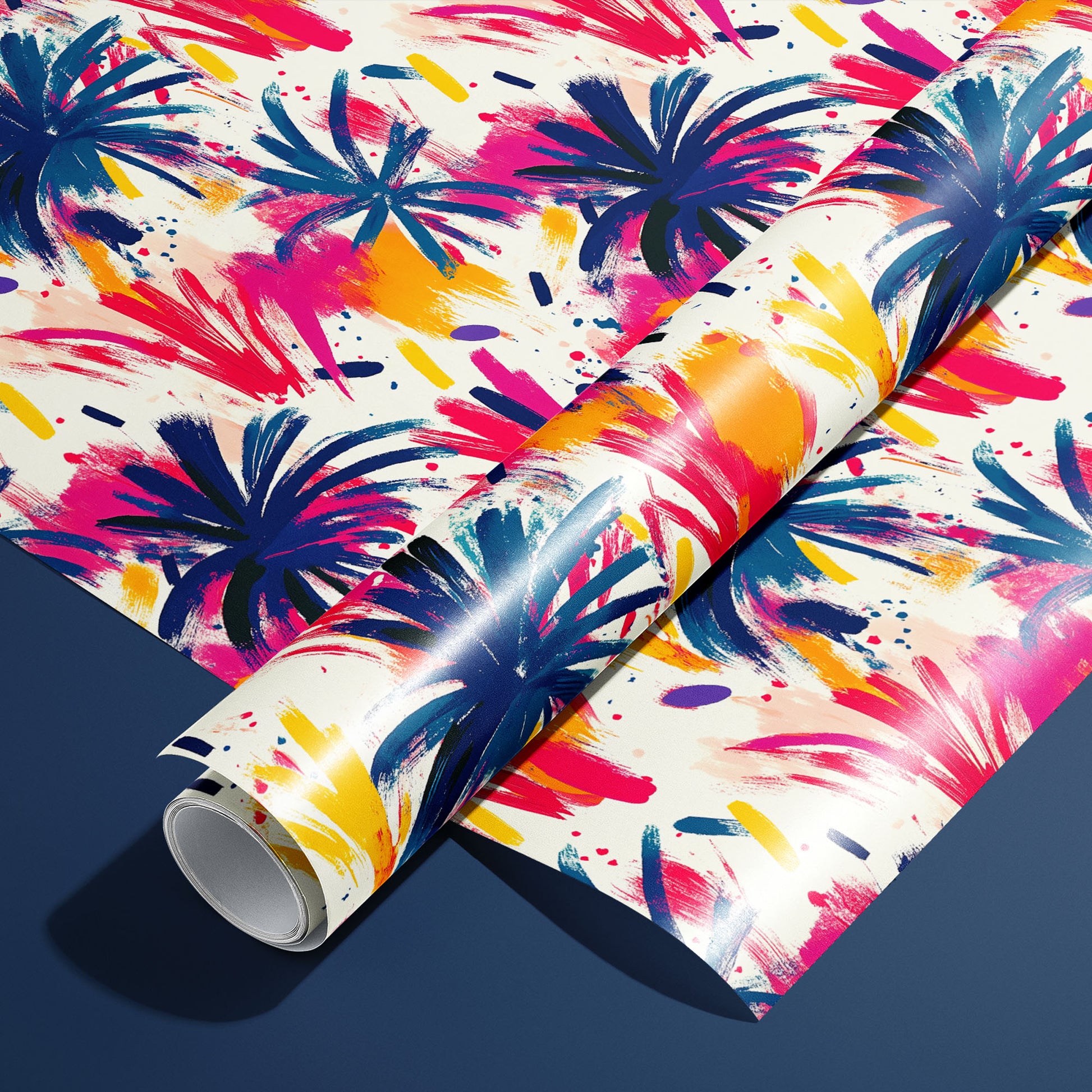 A roll of Artful Fireworks paper on a matching unrolled sheet shows painterly firework bursts with lively brushstrokes and splashes in magenta, cobalt, and gold on cream, resting on a navy blue surface.