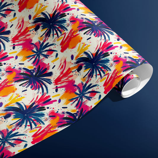 A partially unfurled roll of Artful Fireworks wrapping paper reveals expressive brushstroke fireworks and paint splatters in magenta, cobalt, and gold on cream, against a navy blue background.