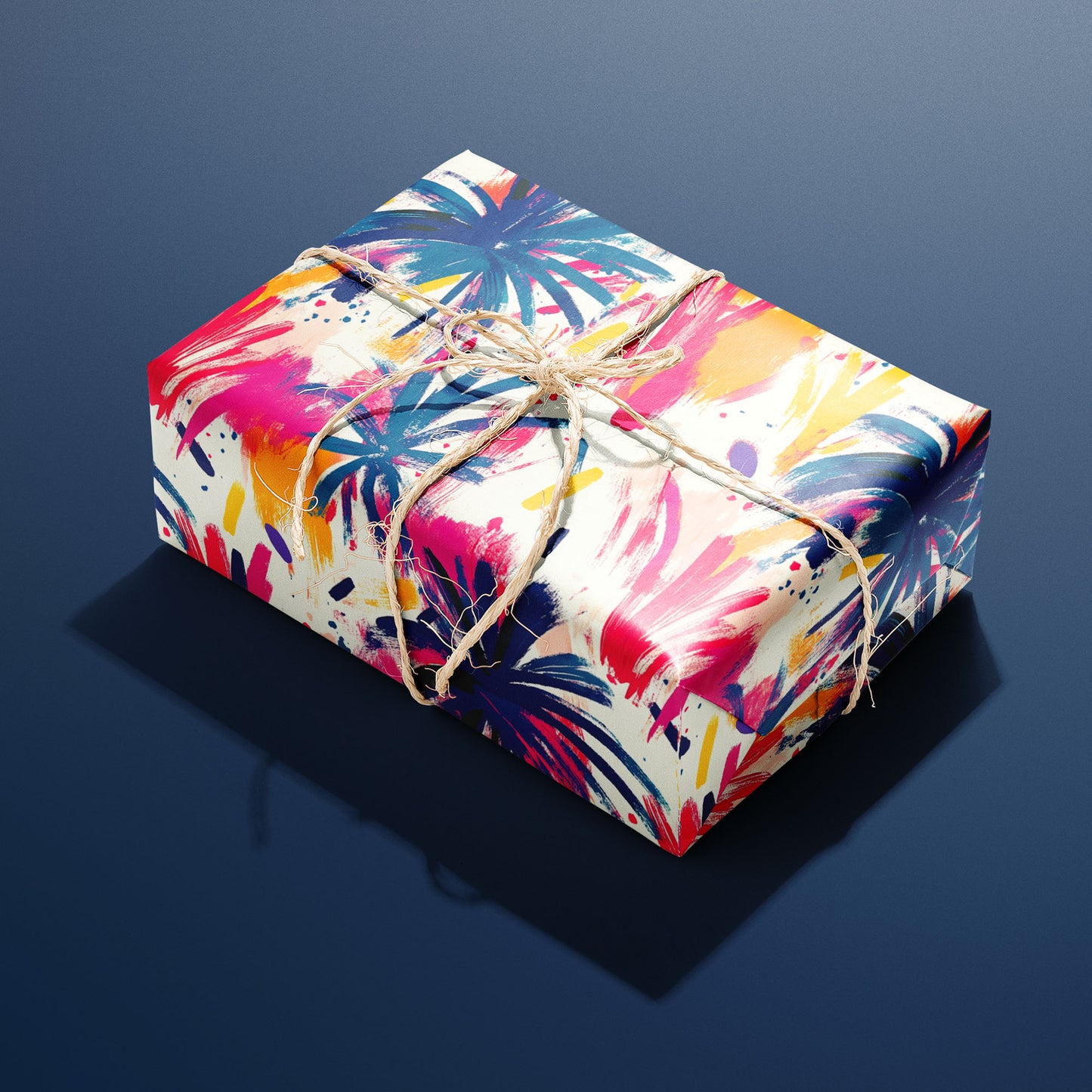 A rectangular gift wrapped in Artful Fireworks paper and tied with natural twine displays bold brushstroke fireworks in magenta, cobalt, and gold on cream resting a navy blue background.