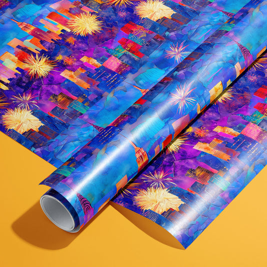 A roll of Electric Cityscape paper on a matching unrolled sheet shows neon city skylines with fireworks over painterly blues and purples, photographed on a mustard orange background.