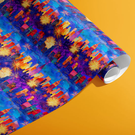 A partially unfurled roll of Electric Cityscape wrapping paper reveals neon skyline silhouettes and fireworks across painterly blues and purples on a mustard orange background.
