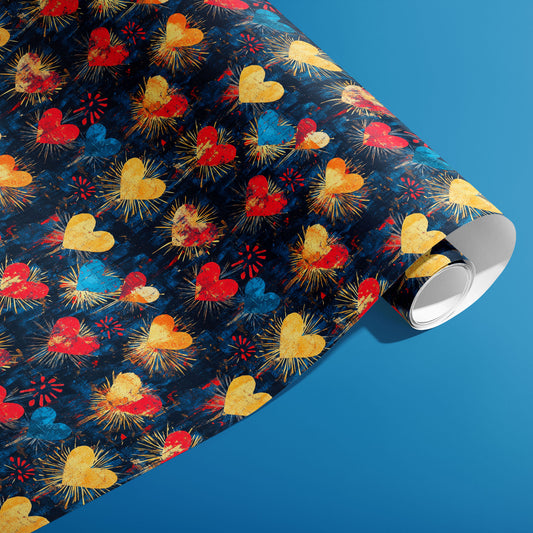 A partially unfurled roll of Radiant Hearts gift wrap reveals grunge-textured hearts and radiant bursts on a dark navy ground against a bright blue background.