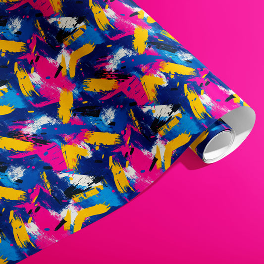 A partially unfurled roll of Electric Splash wrapping paper reveals neon brushstroke splashes in magenta, yellow, and cobalt with black dashes and white flecks on a hot pink background.
