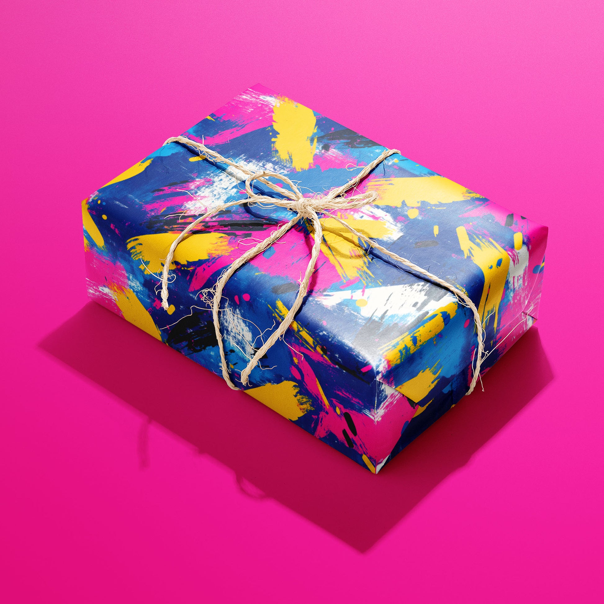 A rectangular gift wrapped in Electric Splash paper and tied with natural twine shows neon magenta, yellow, and cobalt brushstrokes with black dashes on a hot pink background.