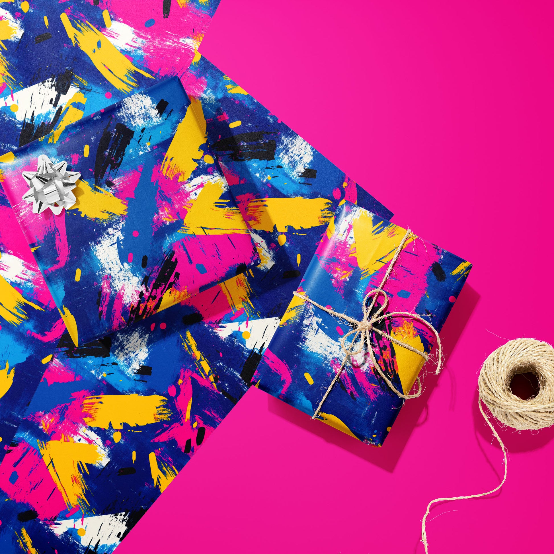 Two gifts in Electric Splash—one with a silver bow and one tied with twine—rest on unused sheets of the neon brushstroke print next to a twine spool on a hot pink background.