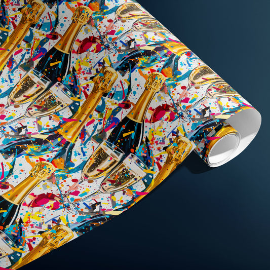 A partially unfurled roll of Glitter & Fizz wrapping paper reveals glittering confetti and bubbly motifs with champagne bottles and flutes on white, resting against a charcoal gray background.