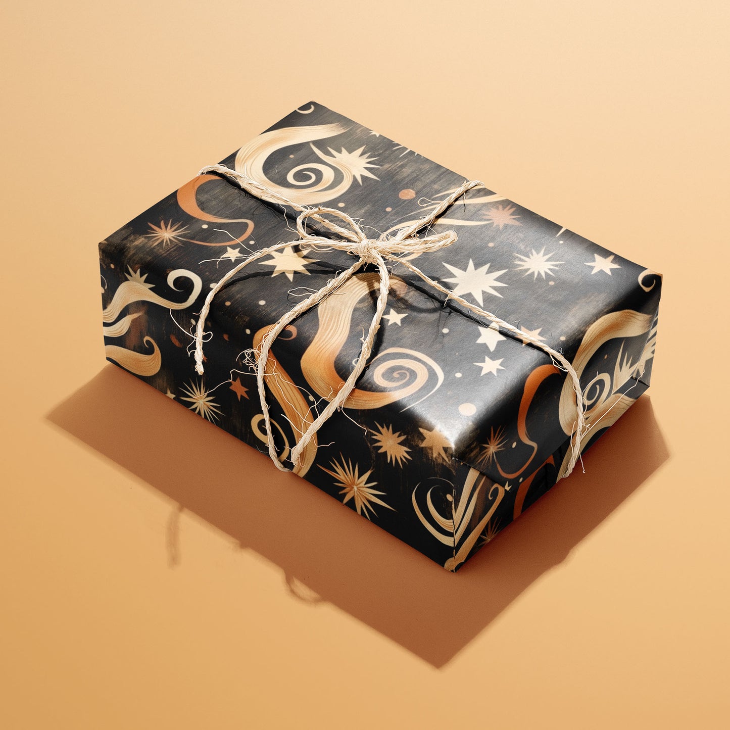 A rectangular gift wrapped in Golden Stardust’s starry, swirling celestial pattern and tied with a natural twine bow on a warm peach background.