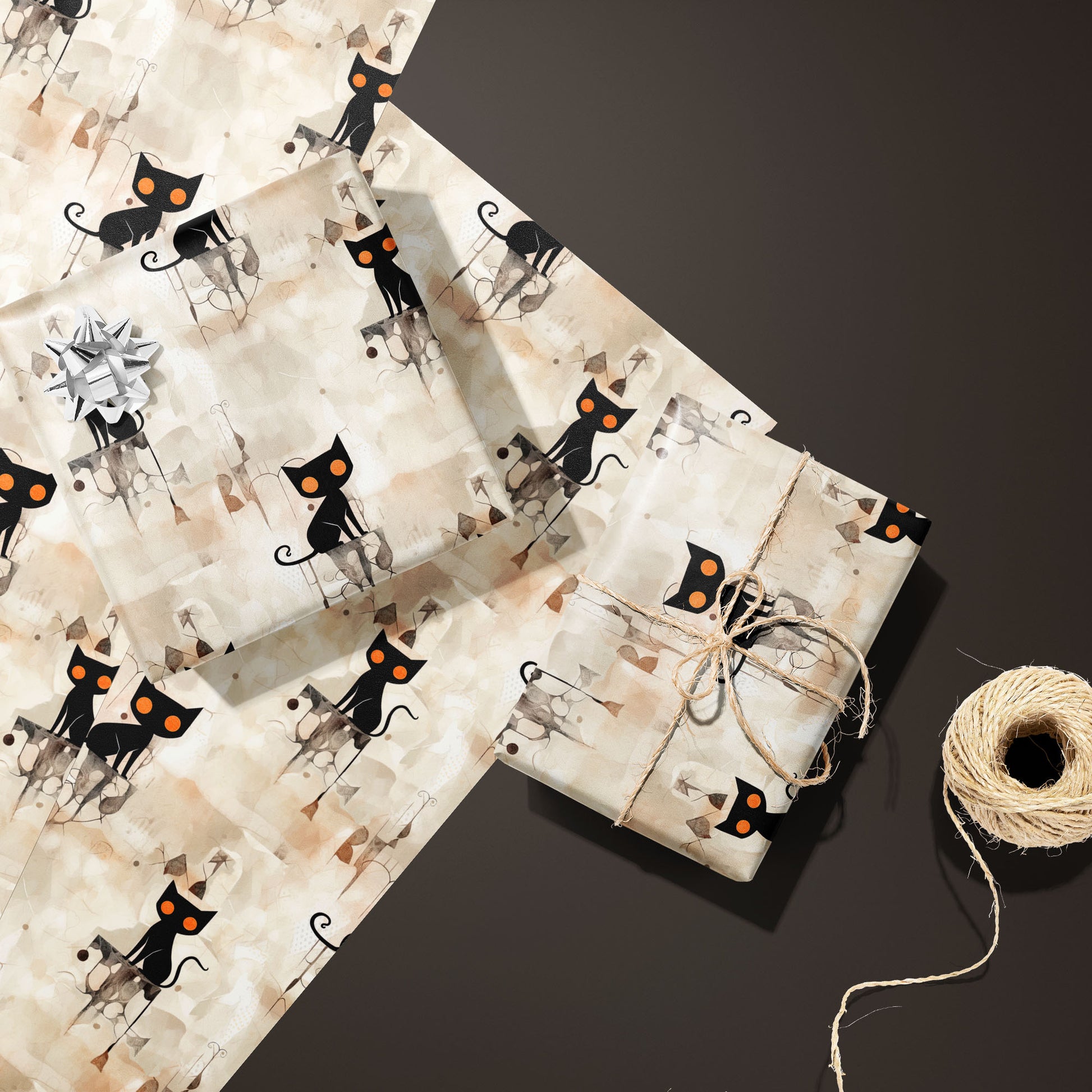 Two gifts in Contemporary Black Cats—one with a silver bow and one tied with twine—rest on unused sheets of the orange-eyed cat print beside twine on a deep espresso background.