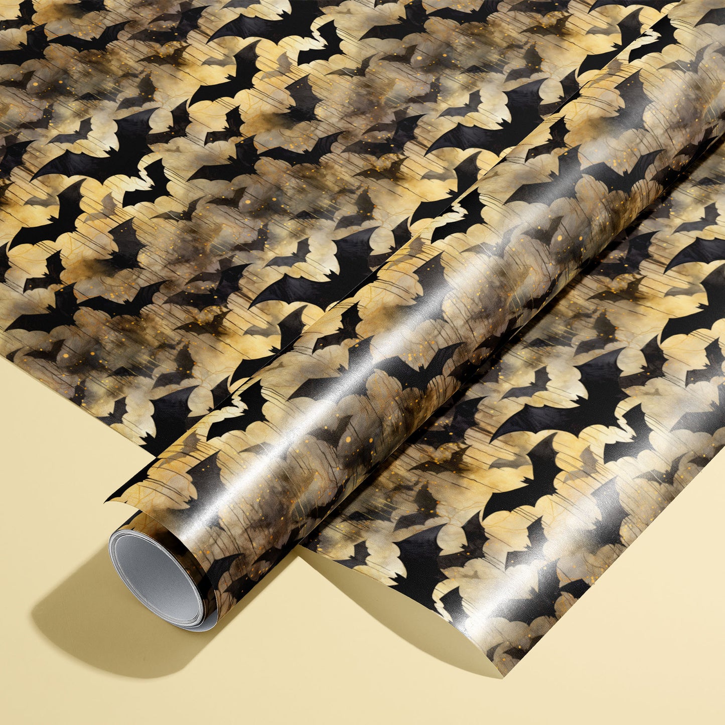 A roll of Spooky Black Bats wrapping paper resting on a matching unrolled sheet, featuring black bat silhouettes over moody gold watercolor textures on a pale yellow background.