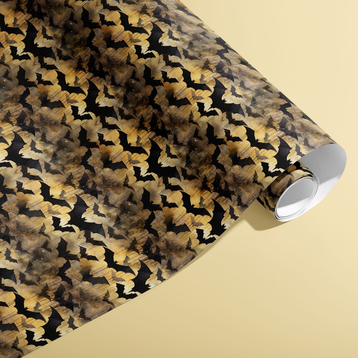 A partially unfurled roll of Spooky Black Bats giftwrap showing inky bat motifs with golden, smoky watercolor washes against a pale yellow surface.