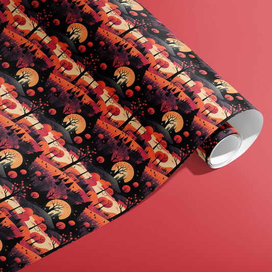 A partially unfurled roll of Halloween Landscape giftwrap showing haunted hills, bare trees, and glowing moons in deep orange tones on a coral-red surface.