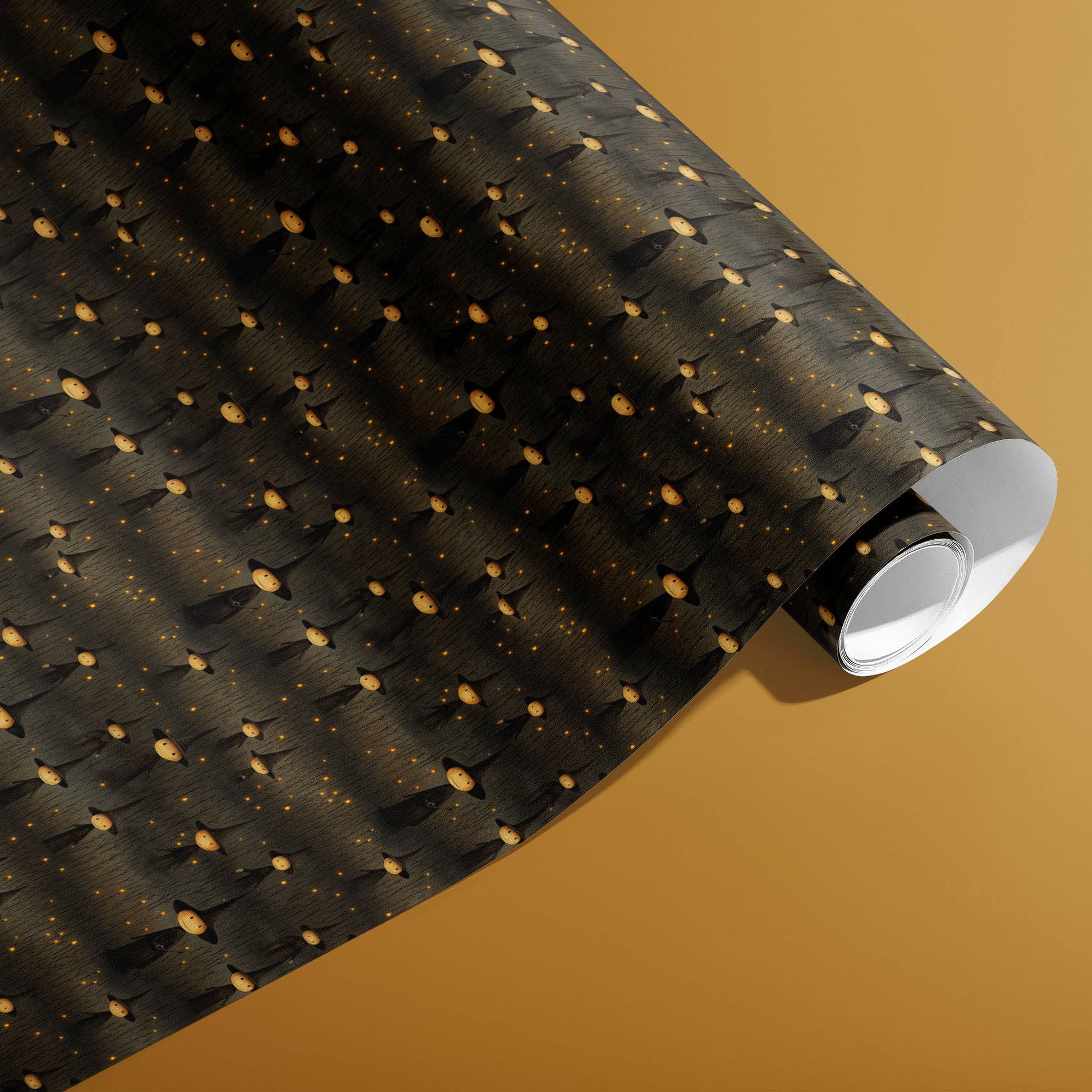 A partially unfurled roll of Halloween Witches wrap showing round-faced witches and glowing specks over a charcoal woodgrain on a warm mustard background.