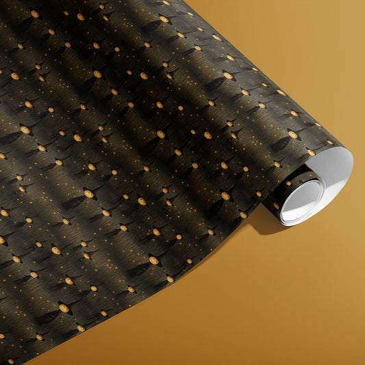 A partially unfurled roll of Halloween Witches wrap showing round-faced witches and glowing specks over a charcoal woodgrain on a warm mustard background.