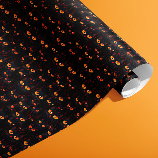 A partially unfurled roll of Cat’s Eyes gift wrap displays luminous cat eyes and sleek black cat faces on a dark ground against a bright orange background.