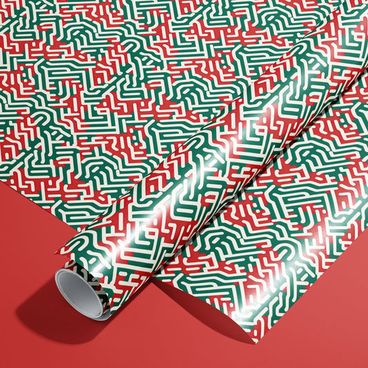 A roll on an unrolled sheet of Geometric Xmas wrapping paper featuring maze-like red, green, and white linework on a satin finish, set on a rich red background.