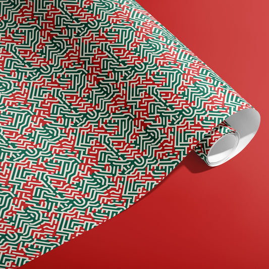 A partially unfurled roll of Geometric Xmas wrapping paper with abstract labyrinthine red, green, and white paths displayed on a red backdrop.