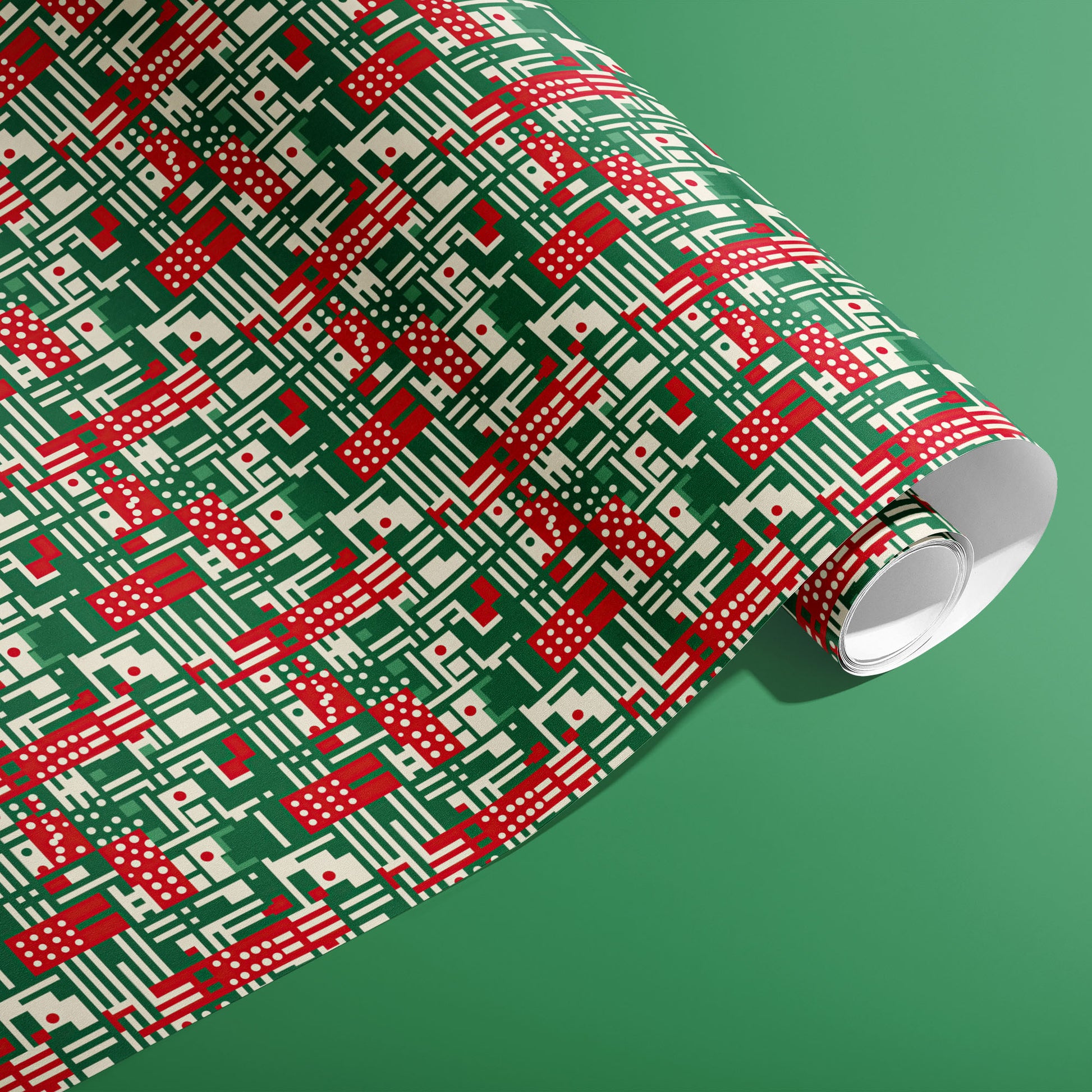 A partially unfurled roll of Abstract Christmas wrapping paper with red, green, and cream geometric stripes, dots, and grid lines on a green background.