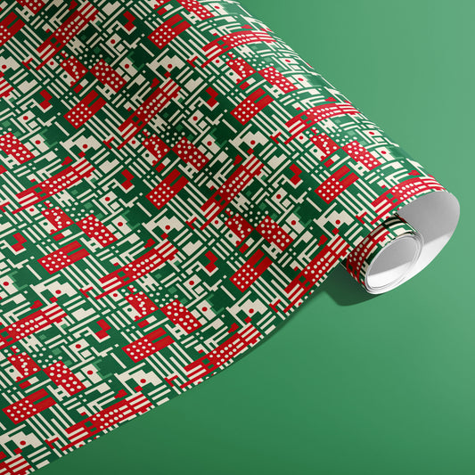 A partially unfurled roll of Abstract Christmas wrapping paper with red, green, and cream geometric stripes, dots, and grid lines on a green background.