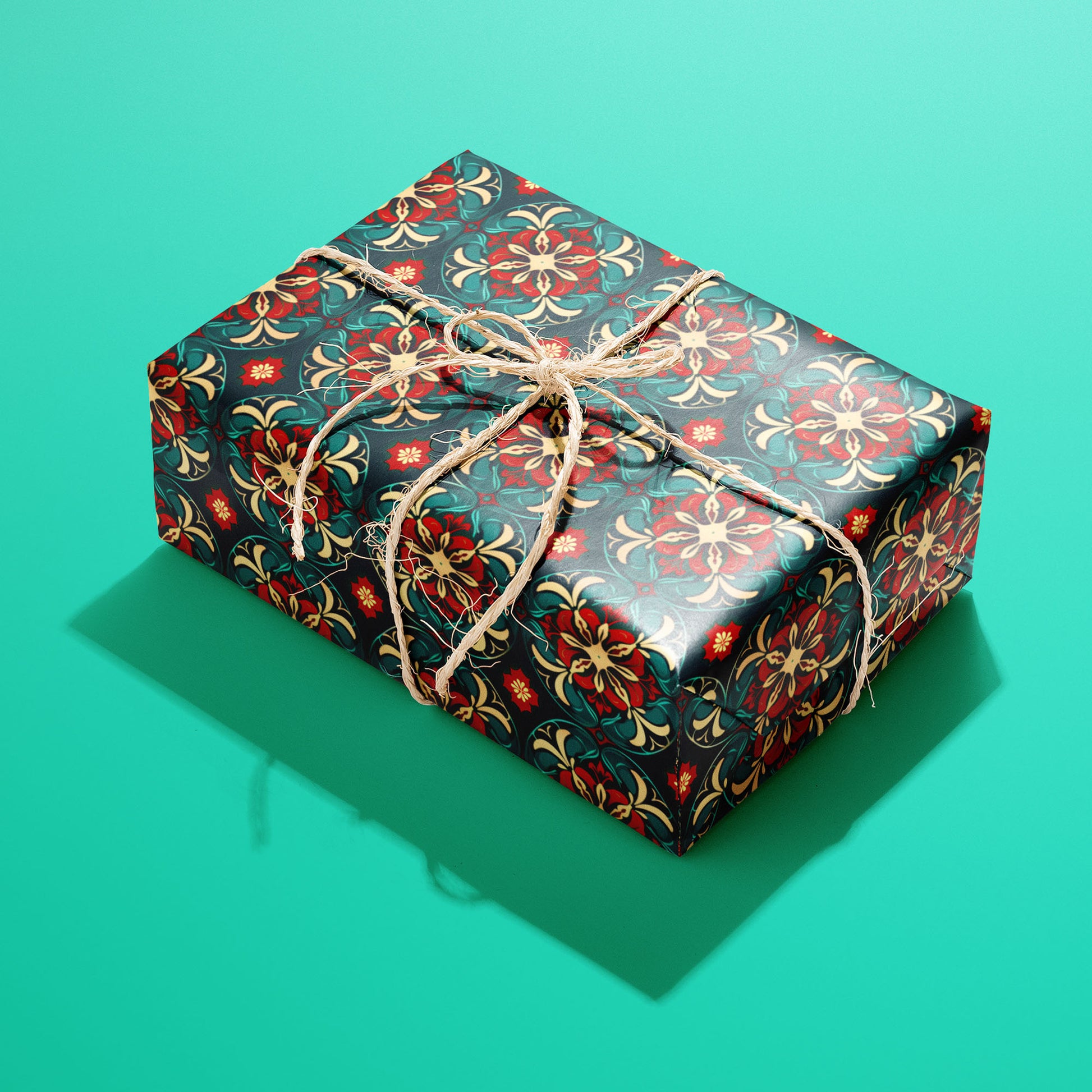A single rectangular gift wrapped in Arabesque Christmas paper, the red and gold arabesque tile pattern tied with natural twine on a bright teal background.