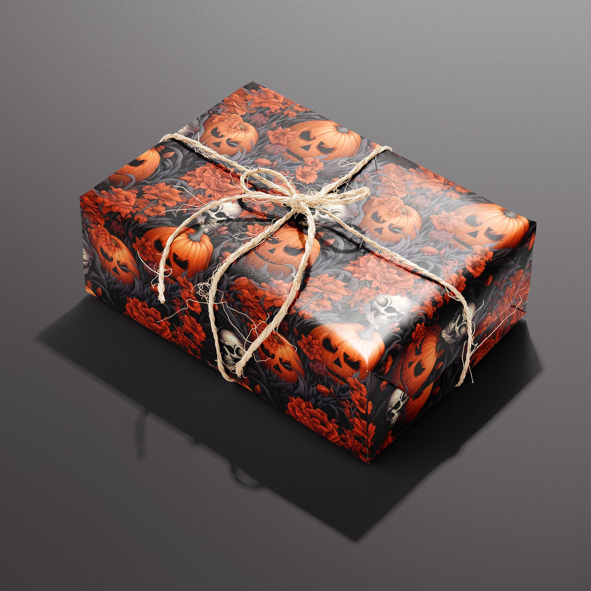 A single rectangular gift wrapped in Ghastly Grove and tied with natural twine, its pumpkins, skulls, and red flowers in dark leaves gleaming against a black print on a dark gray background.