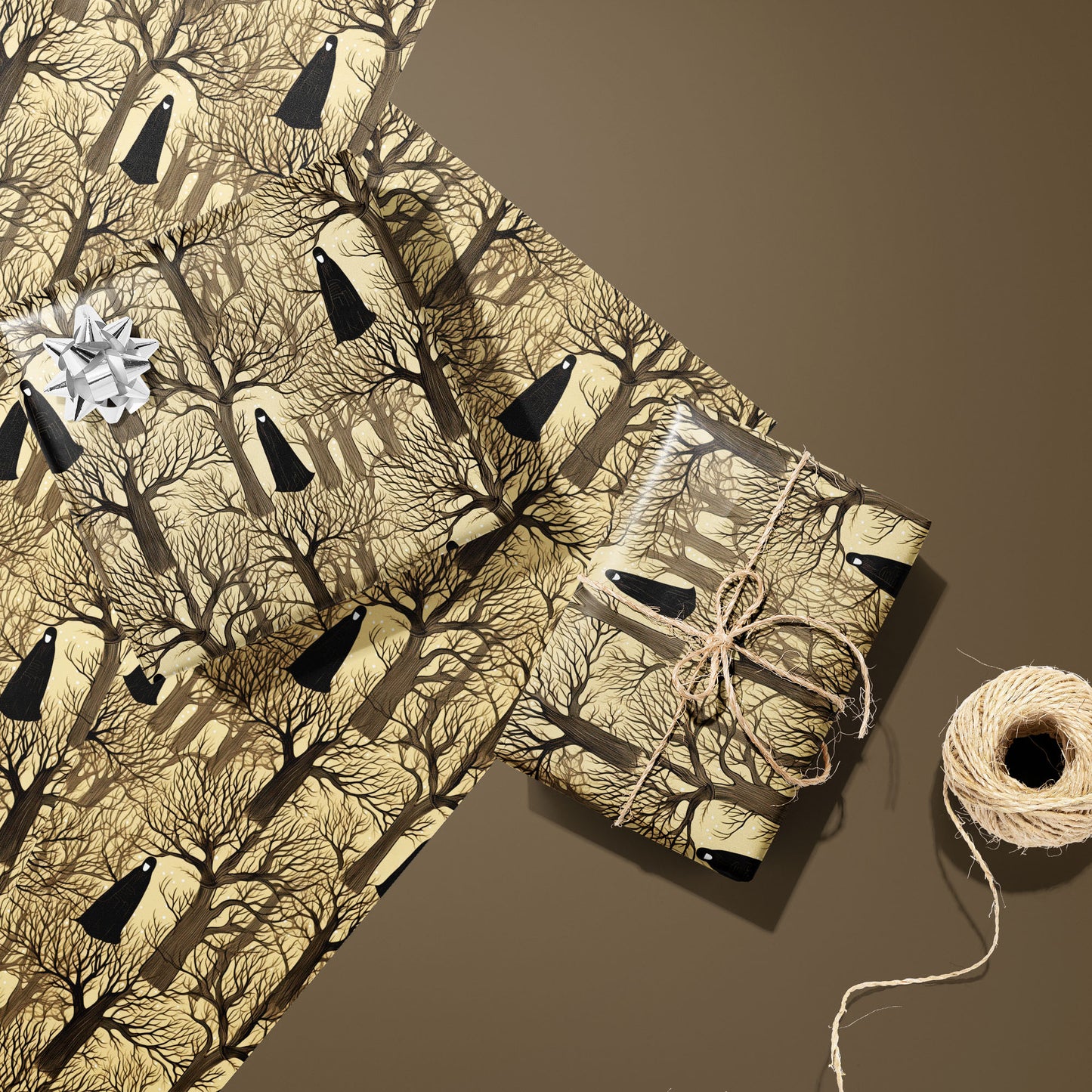 Two Silent Forest gifts—one with a silver bow and one tied with twine—rest on two unused sheets beside a twine spool on a warm brown surface, showing cloaked figures and bare trees.