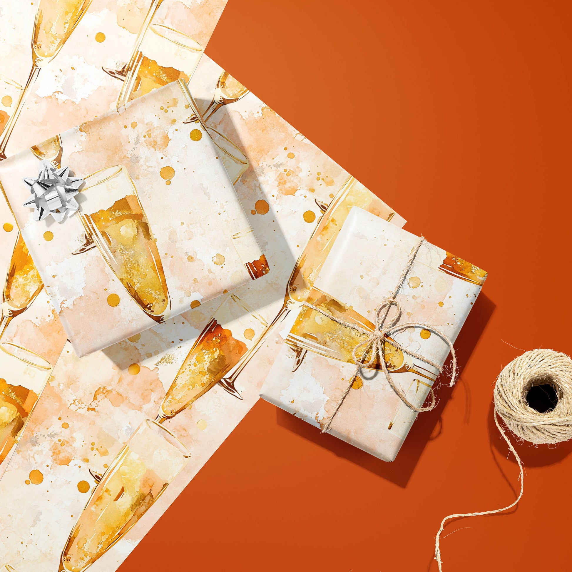 Two gifts in Sparkling Celebrations—one silver-bowed and one tied with twine—rest on two unused sheets with bubbly champagne flutes on blush cream beside twine on orange.