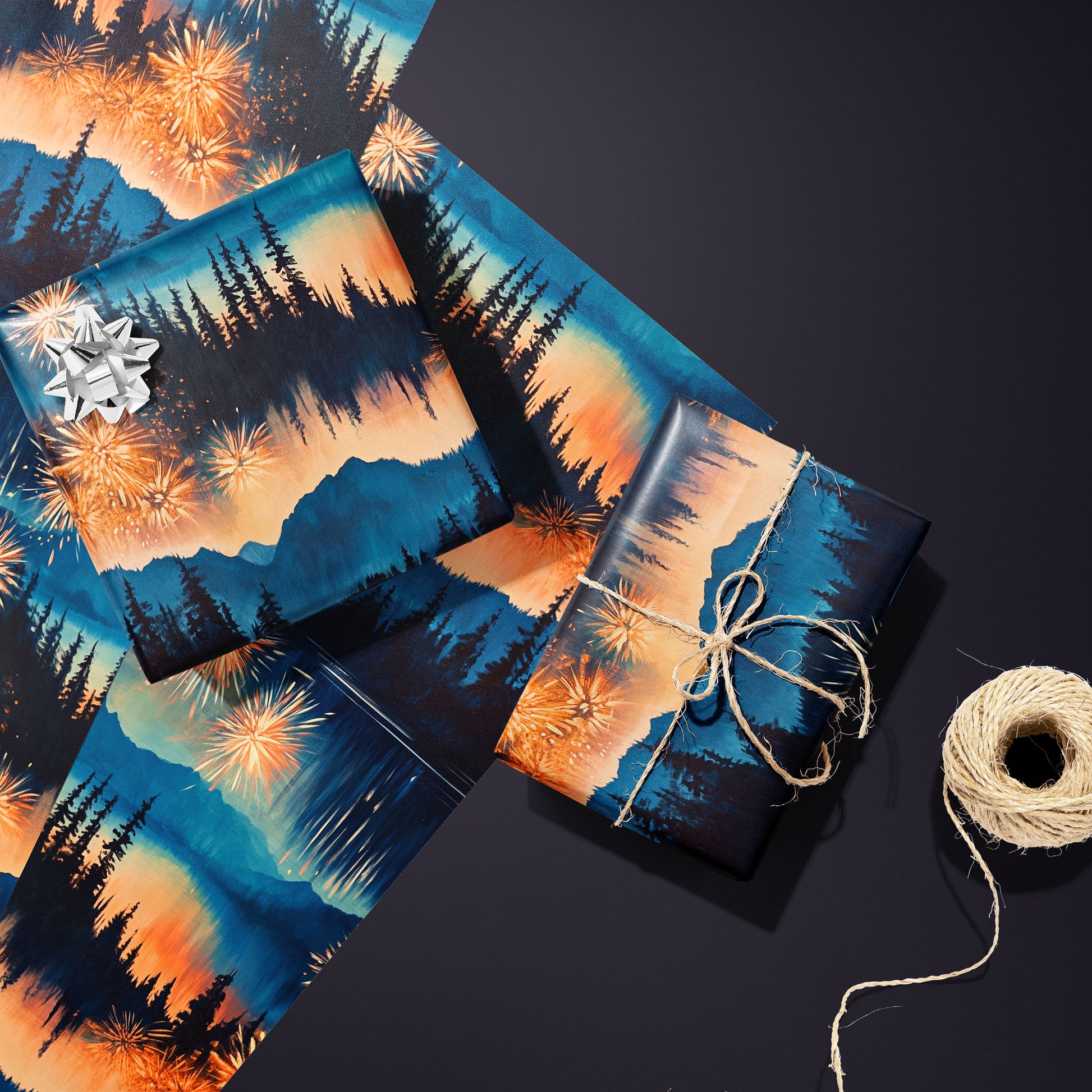 Two gifts in Radiant Reflections—one silver-bowed and one tied with twine—rest on two unused sheets showing fireworks and pine silhouettes beside a twine spool on a charcoal-purple surface.