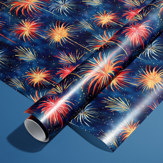 A roll of Blooming Sky wrapping paper resting on an unrolled sheet, with painterly fireworks bursts in red, gold, and white on a midnight navy print, on a steel-blue background.