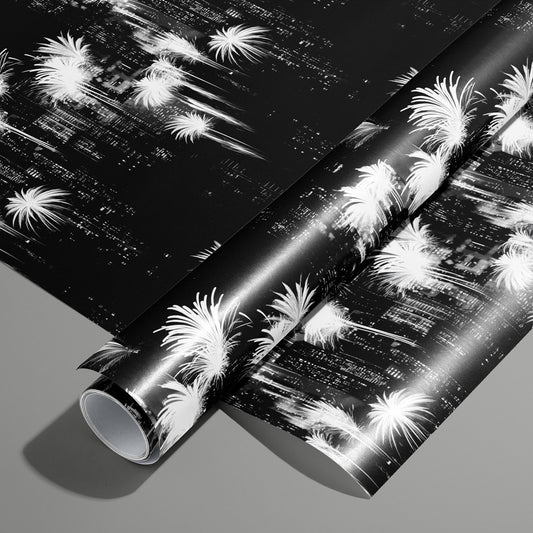 A roll on an unrolled sheet of Fireworks Fantasy black-and-white design wrapping paper with radiant fireworks and spark trails on inky black, set on a slate gray background.
