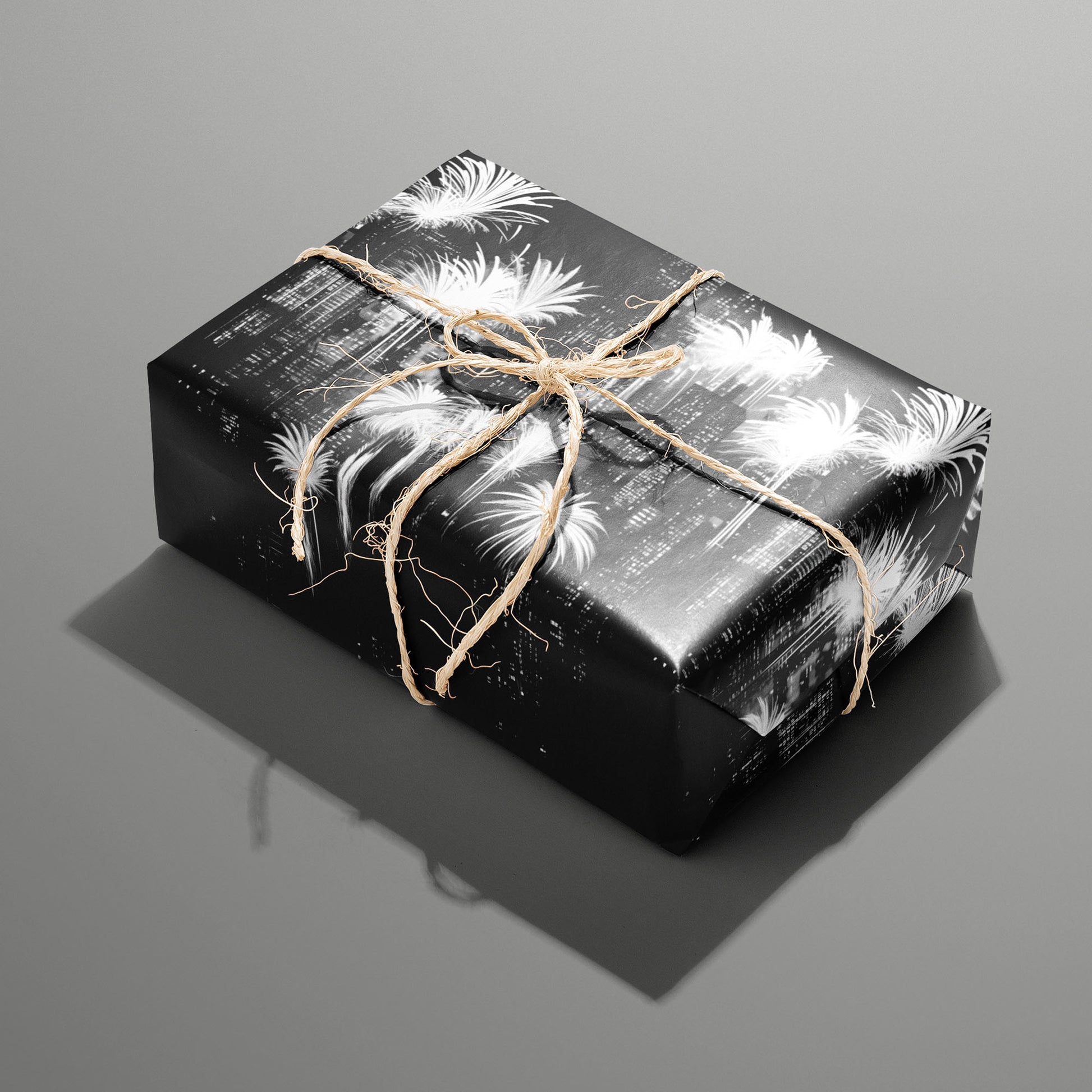 A single rectangular gift wrapped in Fireworks Fantasy paper—bright white fireworks bursts on black—tied with natural twine on a slate gray background.