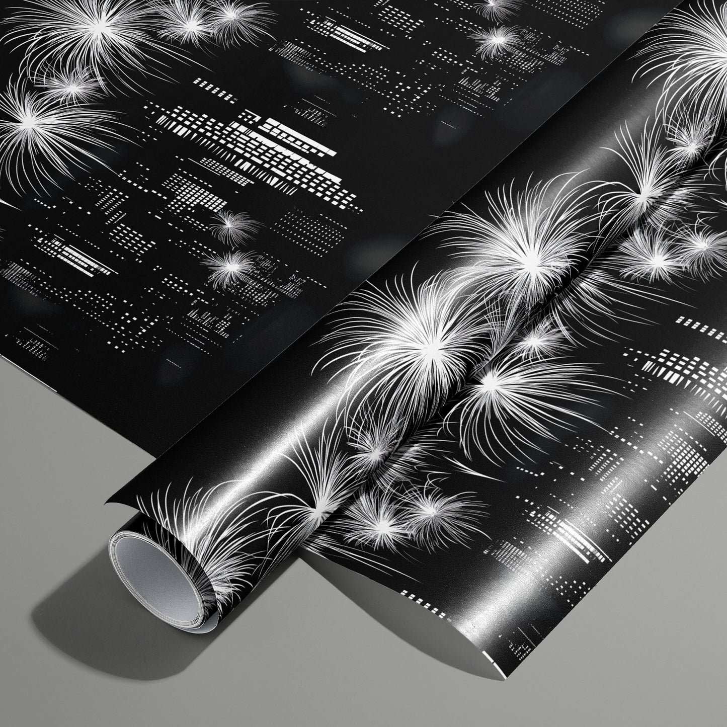 A roll of Skyline Magic wrapping paper on an unrolled sheet, showing a black-and-white city skyline with fireworks and geometric building lights, on a medium gray surface.