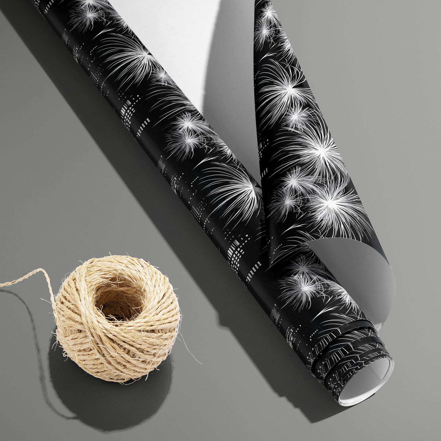 A partially unfurled roll of Skyline Magic with the white underside visible beside a spool of natural twine, showing white fireworks over a black cityscape on a medium gray surface.