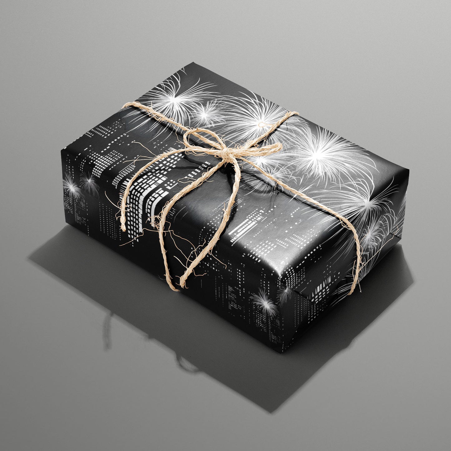 A single rectangular gift wrapped in Skyline Magic and tied with natural twine, its black-and-white skyline and fireworks motif gleaming on a medium gray background.