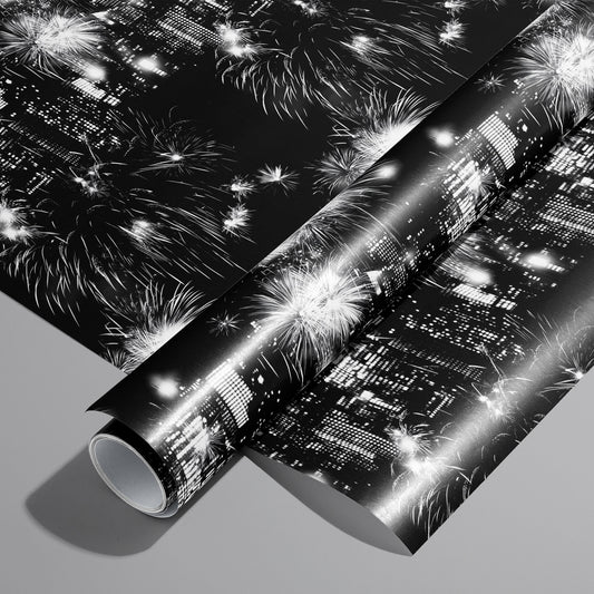 A roll on an unrolled sheet of Skyline Celebration wrapping paper with monochrome city skylines and bursting fireworks on black, set on a cool gray background.