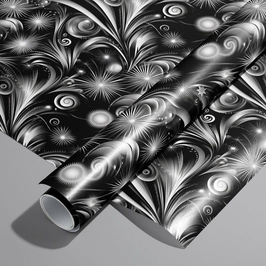 A roll of Fireworks Finale wrapping paper resting on an unrolled sheet, with grayscale starbursts, spirals, and comet-like arcs on black, set on a medium gray background.