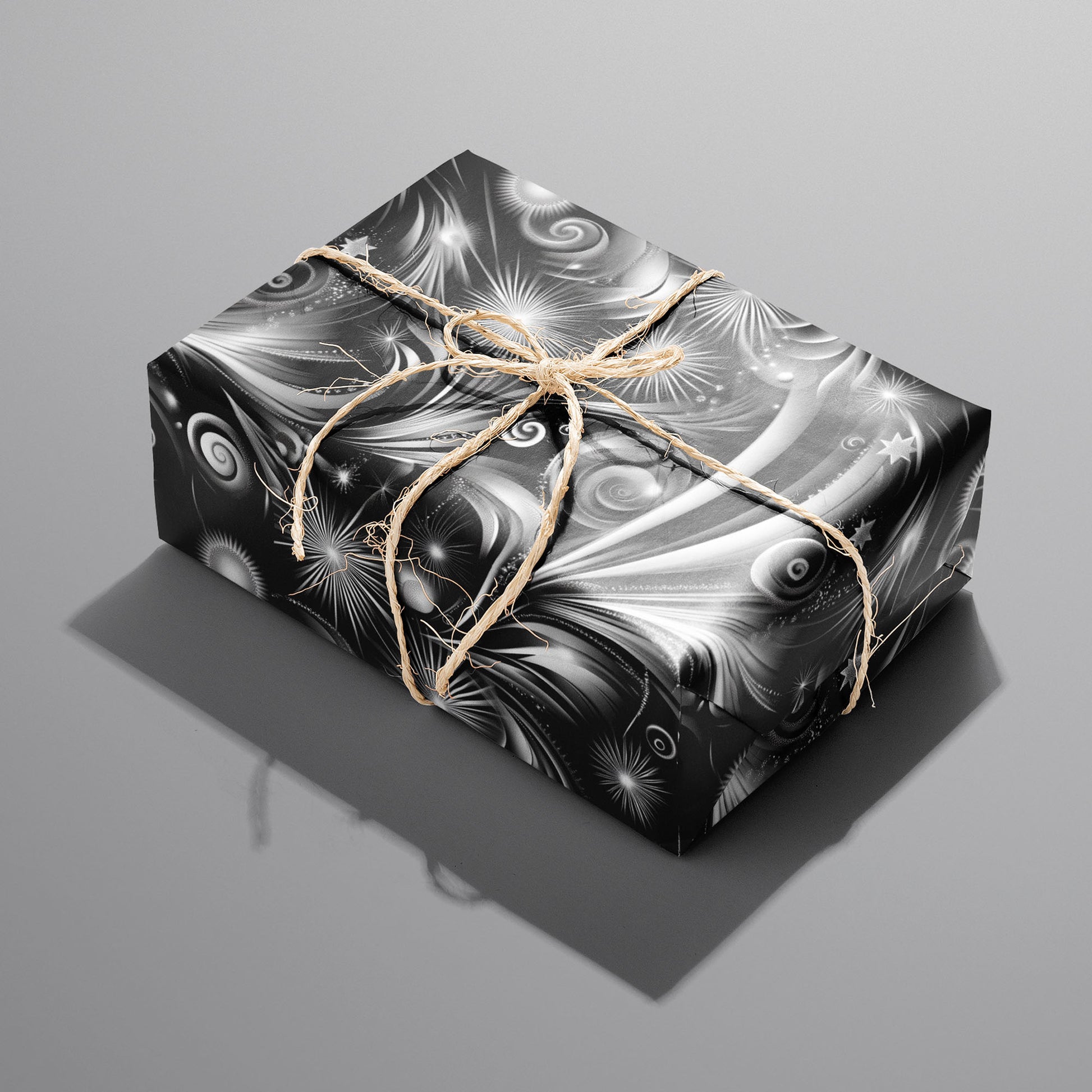 A single rectangular gift wrapped in Fireworks Finale and tied with natural twine, its black-and-white starbursts and sweeping trails shining on a medium gray background.