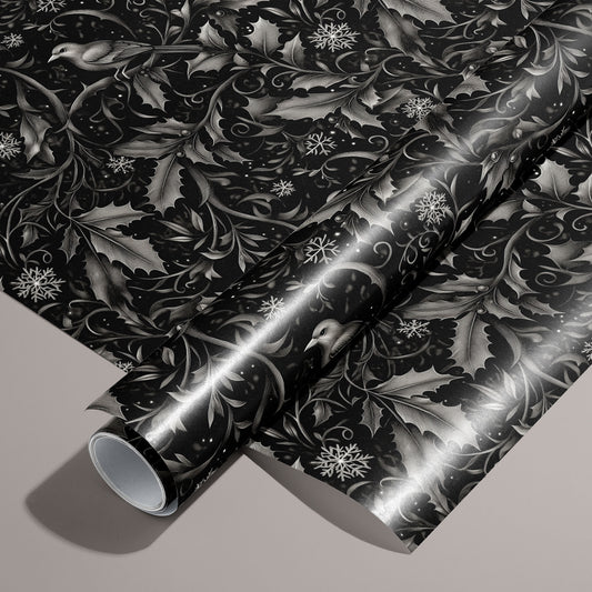 A roll of Winter Song wrapping paper rests on a matching unrolled sheet, featuring monochrome songbirds, holly leaves, and snowflakes on a black field over a warm taupe background.