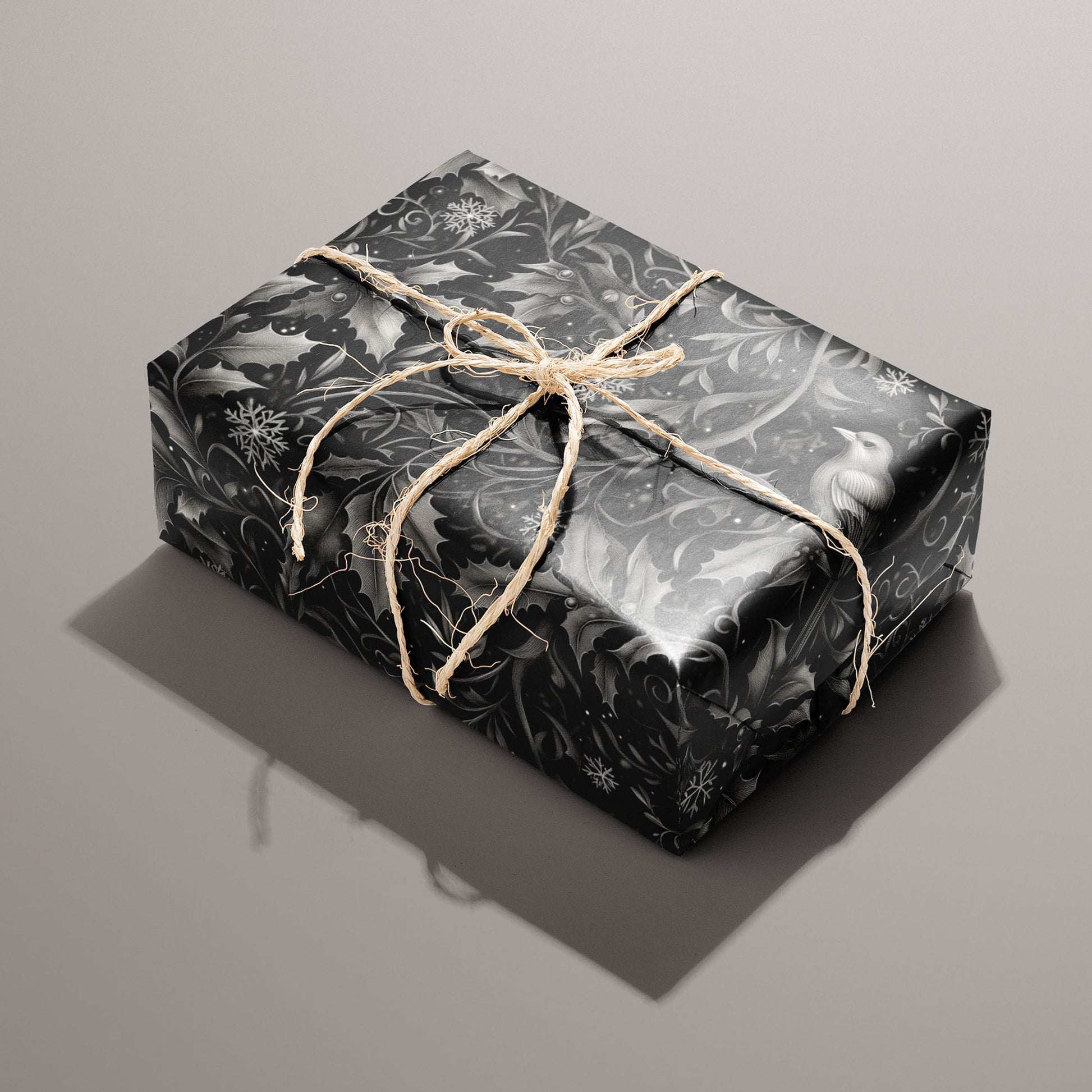 A single gift wrapped in Winter Song and tied with natural twine displays monochrome birds, holly foliage, and snowflakes on a black ground against a taupe background.
