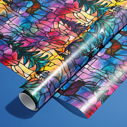 A roll on an unrolled sheet of Majestic Nightfall wrapping paper with stained-glass deer and pine boughs in jewel tones outlined in black, set on a cobalt blue background.