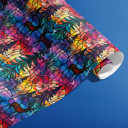 A partially unfurled roll of Majestic Nightfall wrap showing multicolor stained-glass deer and fir fronds with black leading on a cobalt blue background.